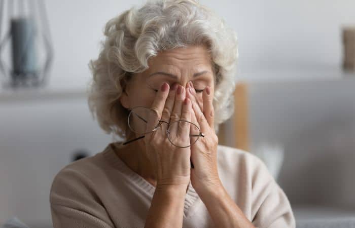 older woman pressing eyes closed holding glasses