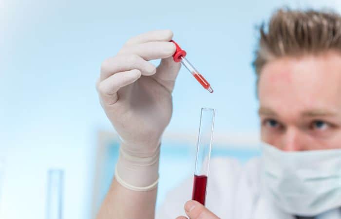 man holding test tube and dropper filled with red chemical