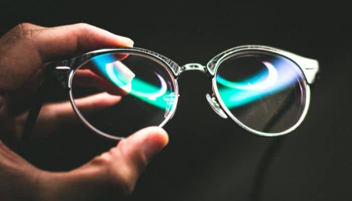 hand holding eyeglasses with light reflecting off lenses