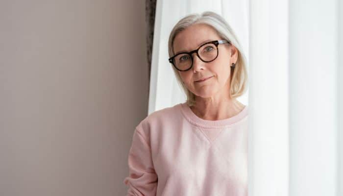 mature woman wearing glasses standing near curtain