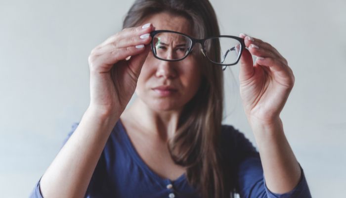 woman holding eyeglasses away from face