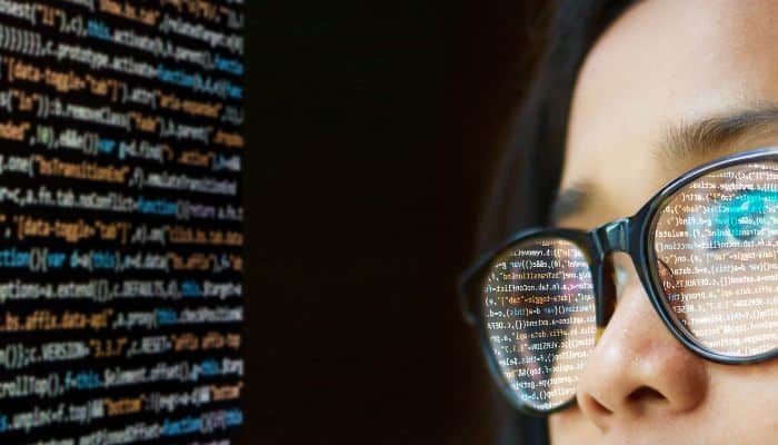 woman with computer screen text reflecting off eyeglass lenses