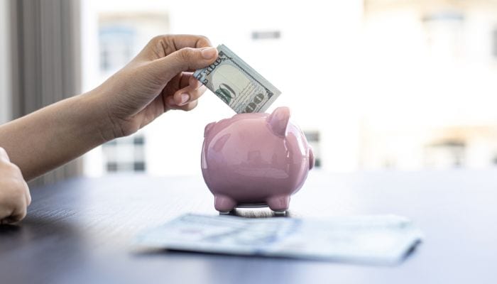 hand inserting $100 bill into piggy bank