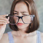 squinting woman holding eyeglasses off face