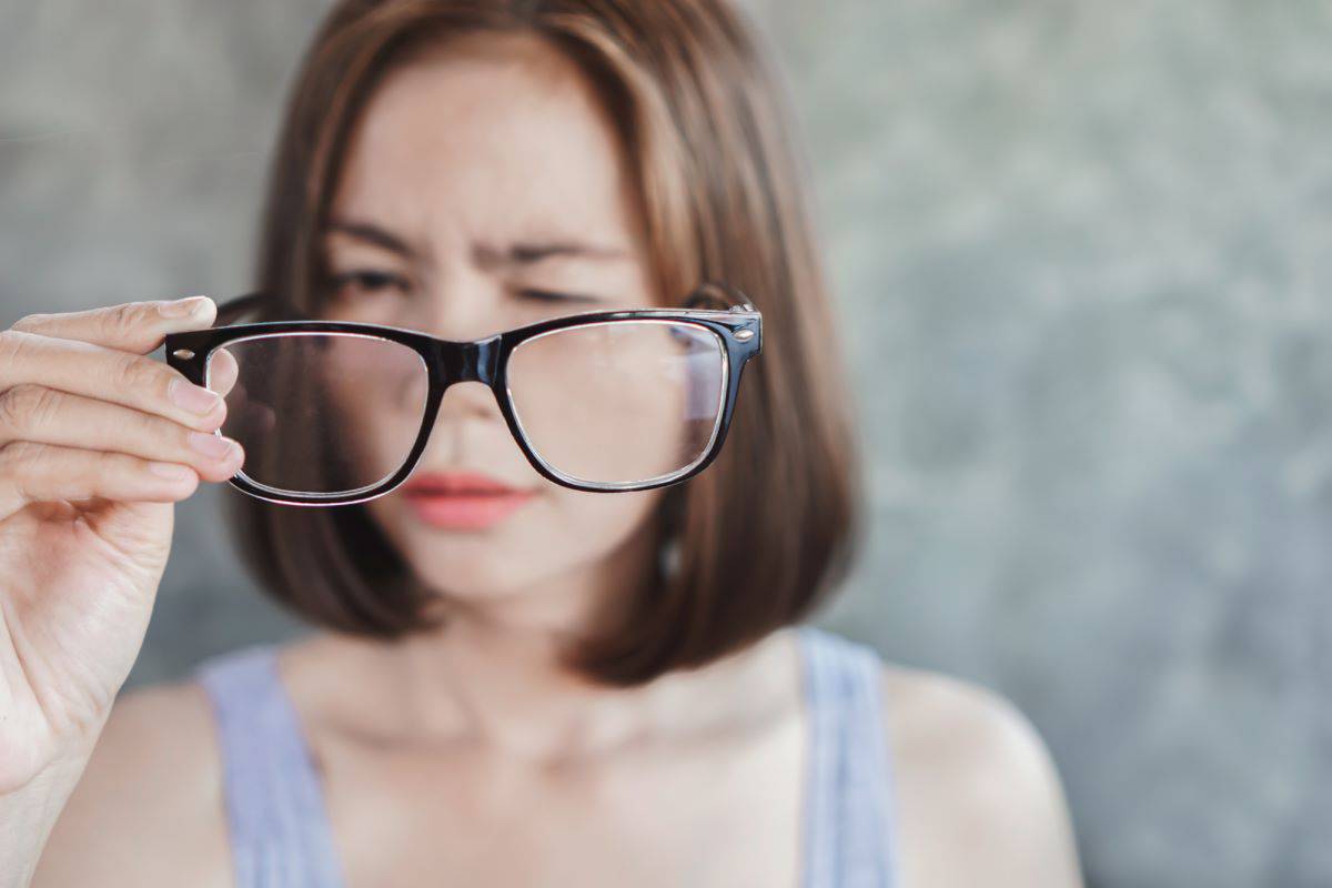 squinting woman holding eyeglasses off face