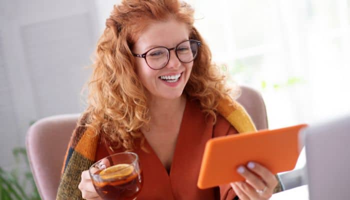 woman in glasses holding cup of tea and a tablet