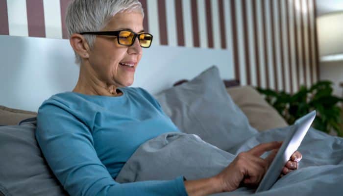 woman in bed wearing blue light glasses using tablet